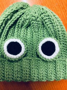 a green knitted hat with two large eyes on top of an orange wooden table