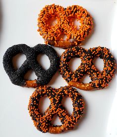 four pretzels with black and orange sprinkles are arranged on a white surface