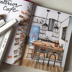 an open book with a drawing of a kitchen in it and two markers next to it