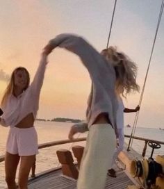 two young women dancing on the deck of a boat at sunset or sunrise, while another woman watches