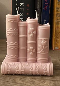 three pink candles sitting on top of a wooden table next to books and a bookcase