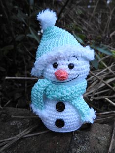 a crocheted snowman sitting on top of a rock wearing a blue hat and scarf