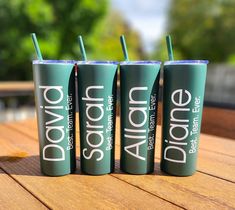 three green tumblers sitting on top of a wooden table with straws in them