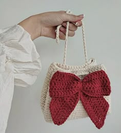 a hand holding a red and white crocheted bag with a bow on it