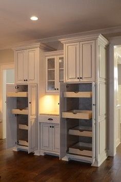 an empty kitchen with white cabinets and wood floors in the middle of it is lit by recessed lights