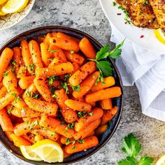 a bowl filled with cooked carrots next to lemon wedges and parsley on the side