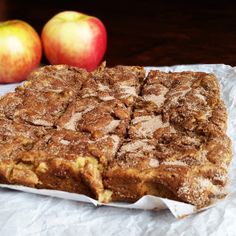 an apple pie sitting on top of a piece of wax paper next to two apples