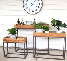 two wooden tables with plants on them in front of a wall clock and white siding