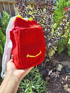 someone is holding up a red knitted bag in front of some bushes and shrubbery