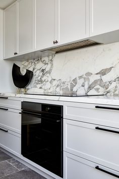 a white kitchen with marble counter tops and black stove top oven, along with cabinets