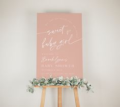 a baby shower sign with greenery on the easel next to an easel