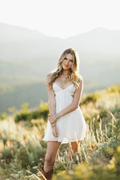 a beautiful young woman in a white dress posing for a photo with mountains in the background