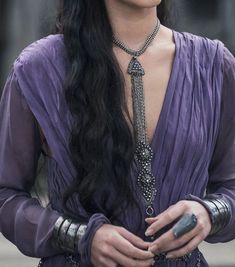 a woman with long black hair wearing a purple dress and holding a cell phone in her hand