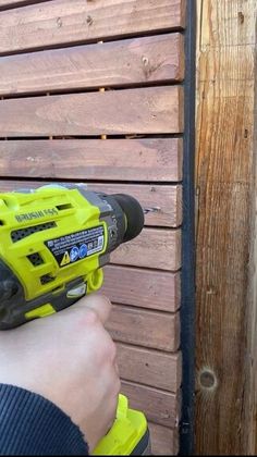 a person is holding a drill in front of a wooden wall with boards on it