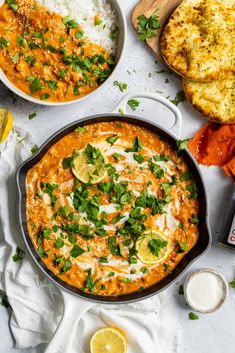 an overhead view of a bowl of red curry with rice, lemons and cilantro