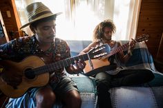 two people sitting on a couch playing guitars