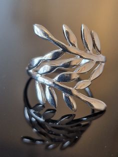 This silver olive leaf ring is a stunning piece of jewelry that features delicate and intricately detailed olive leaves. The ring is crafted from high-quality sterling silver and boasts a polished finish that gives it a bright and lustrous appearance. The olive leaves are sculpted with care, creating a naturalistic effect that makes it seem as if they are freshly picked. The design of this ring is elegant and timeless, making it perfect for wearing with both casual and formal outfits. The olive Leaf Jewellery, Oak Leaf Earrings, Olive Leaf Ring, Greek Ring, Silver Leaf Ring, Woodland Earrings, Olive Leaves, Mystical Jewelry, Handmade Silver Ring