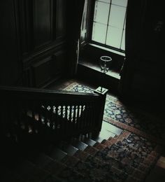 an empty staircase leading up to a window in a dark room with ornate rugs on the floor