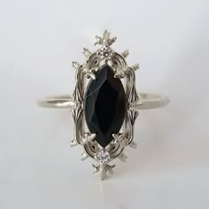 an oval cut black diamond surrounded by leaves and flowers on a white background, set in a silver ring