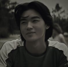 a man with black hair sitting in a park