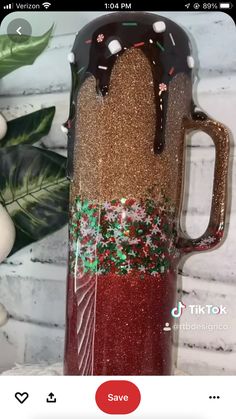 a red and gold coffee cup with chocolate on it, sitting next to a white brick wall