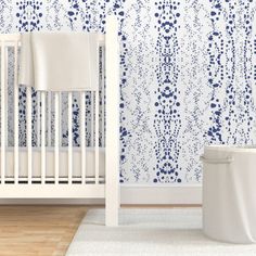 a white crib next to a wall with blue flowers on it and a rug