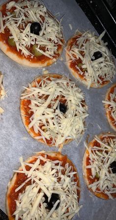 six small pizzas with cheese and olives on them sitting on a baking sheet