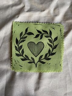 a piece of cloth with a heart on it and leaves around the edges, sitting on a bed sheet