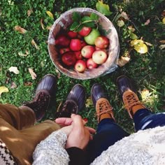 two people sitting on the grass with their feet up in front of a bowl of apples