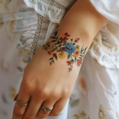 a woman's hand with a flower tattoo on her left wrist and the other arm