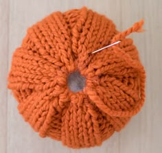 an orange knitted ball with a needle sticking out of it