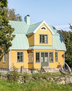 a yellow house with a green roof and two windows on the front, surrounded by trees