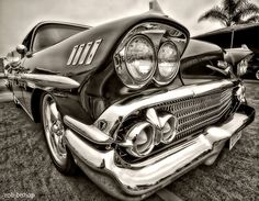 the front end of an old classic car parked in a parking lot with palm trees