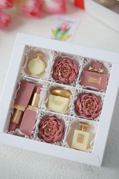 an open white box with pink flowers and perfumes in it