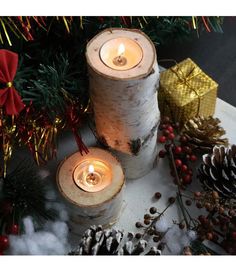 two lit candles sitting on top of a table next to pine cones and christmas decorations