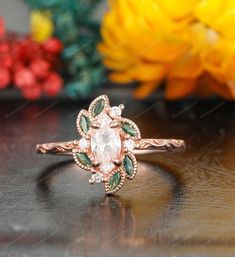 a close up of a ring on a table with flowers in the background and an orange flower behind it