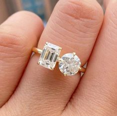 a woman's hand holding an engagement ring with two stones on it, and the other