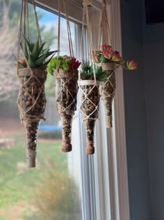 three hanging planters filled with succulents and flowers on a window sill