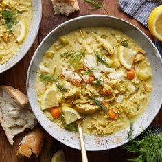 two bowls of chicken noodle soup on a wooden table with bread and lemon slices