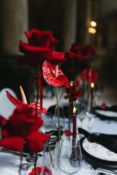 red roses are in vases on a table with white plates and black napkins