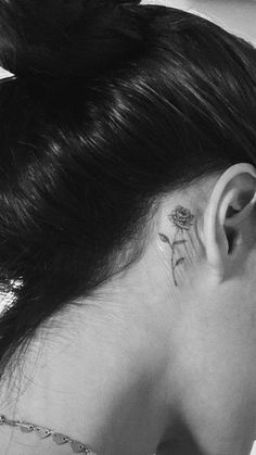 a woman with a flower tattoo on her left side behind the ear is looking down