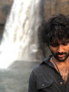 a man standing in front of a waterfall talking on a cell phone while wearing a black shirt