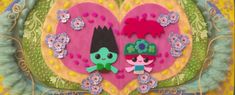 two paper dolls are standing in front of a heart shaped wall decoration with flowers and leaves