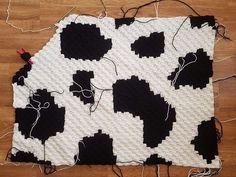 a black and white cow print blanket on a wooden floor with some yarn in it