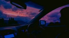 a woman driving in her car at night with the sun going down and dark clouds