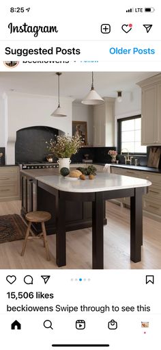 an instagramted photo of a kitchen with white cabinets and dark wood island in the middle