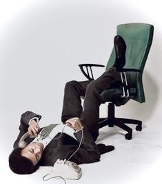 a man laying on the ground next to an office chair with headphones in his ears