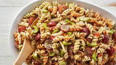 a white bowl filled with pasta salad on top of a wooden table next to a spoon