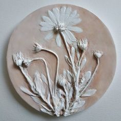 a clay plate with flowers on it sitting on a table next to a white wall