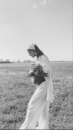 black and white photograph of a pregnant woman in a field with flowers on her belly